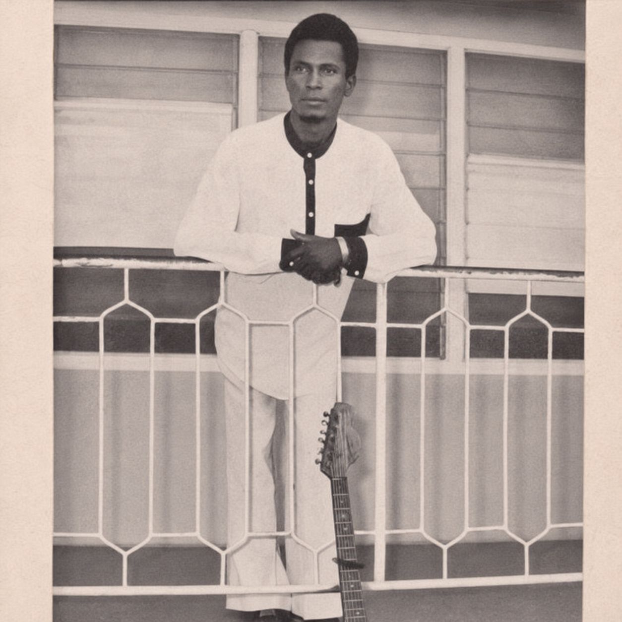 Black and white portrait of Chief Echo Toikumoh standing by a balcony with a guitar